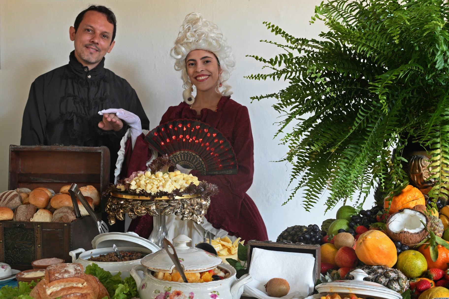 Personagens em trajes de época ao lado de mesa farta